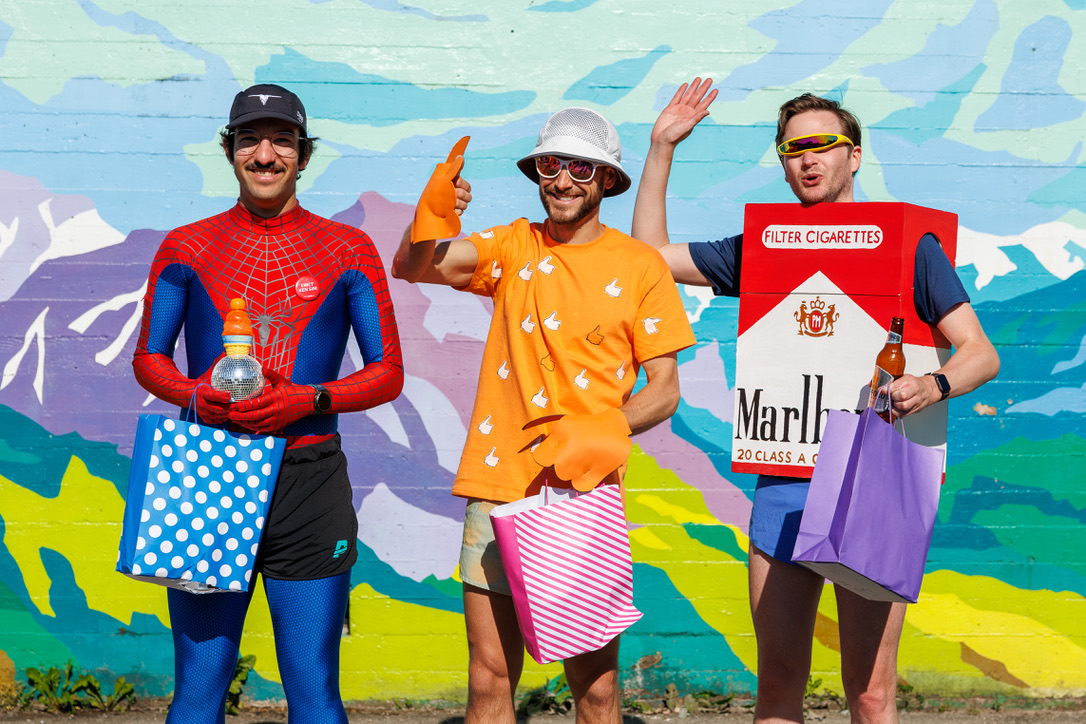 3 people in costumes in a row. Myself, on the left, dressed as Spider-Man, holding a disco ball. 2 other men to my right, dressed as a thumbs-up and a cigarette box, 2nd and 3rd place, respectively.